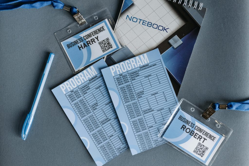Gallery Flat lay of business conference materials including name tags, program, notebook, and pen.